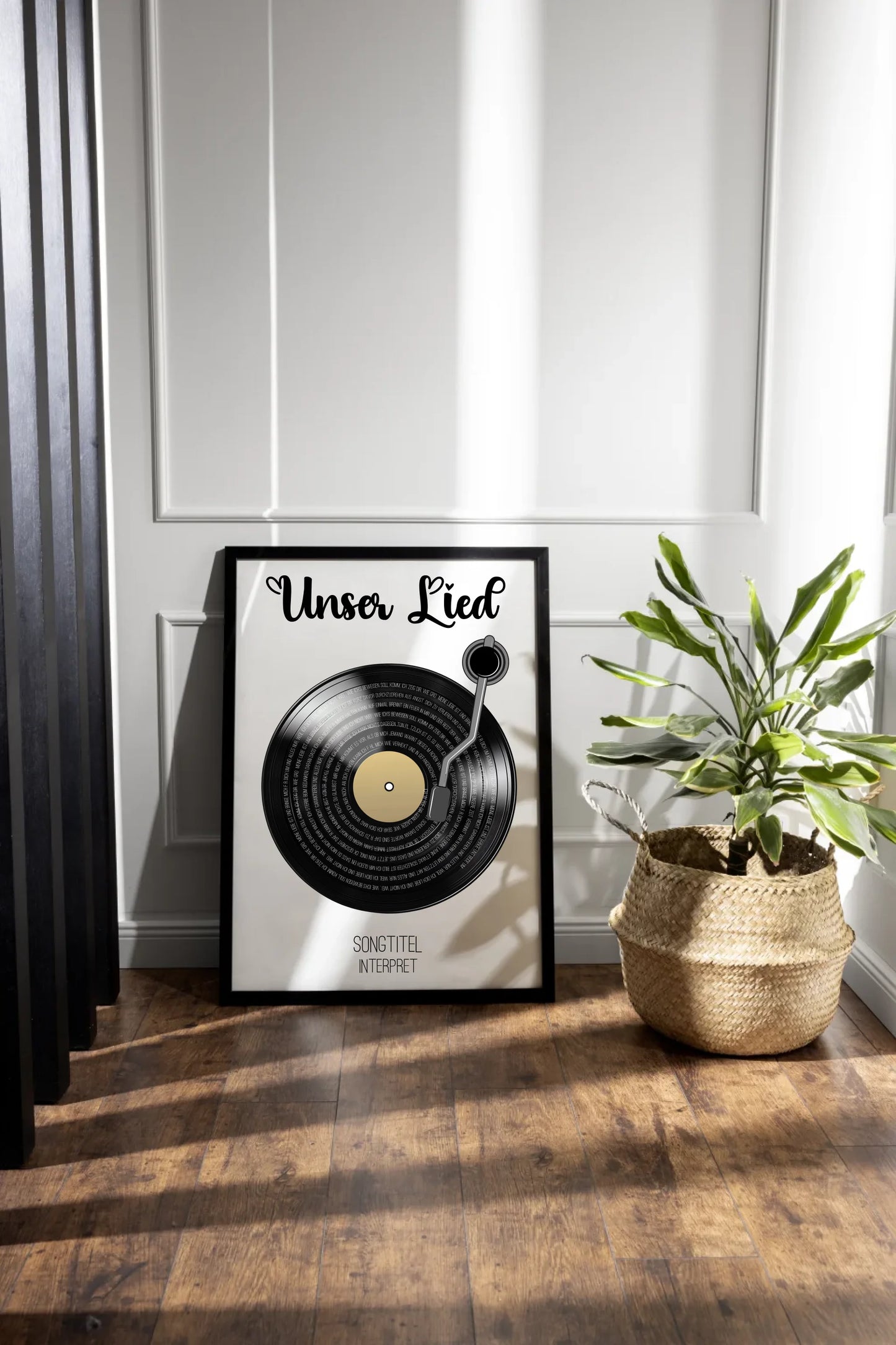 Poster mit Illustration einer schwarzen Schallplatte und Tonarm. Oben steht immer die feste Überschrift ‚Unser Lied‘. Auf den Rillen der Platte wird der ausgewählte Liedtext dargestellt. Unter der Platte erscheinen personalisierbarer Songtitel und Interpret.