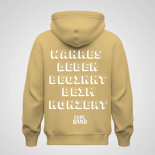 Beiger Hoodie mit großem weißen Schriftzug auf der Rückseite: ‚Wahres Leben beginnt beim Konzert‘. Darunter steht der Schriftzug ‚Eure Band‘. Der Bandname kann individuell angepasst werden.