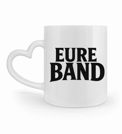 Weiße Keramiktasse mit Herzhenkel und großem schwarzen Schriftzug ‚Eure Band‘ auf der Vorderseite. Der Text kann individuell mit dem eigenen Bandnamen gestaltet werden. 