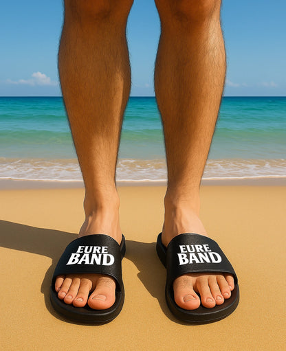 Schwarze Badelatschen mit breitem Riemen. Auf beiden Riemen ist in weißen Buchstaben der Schriftzug ‚Eure Band‘ aufgedruckt. Der Text kann individuell mit dem eigenen Bandnamen gestaltet werden.