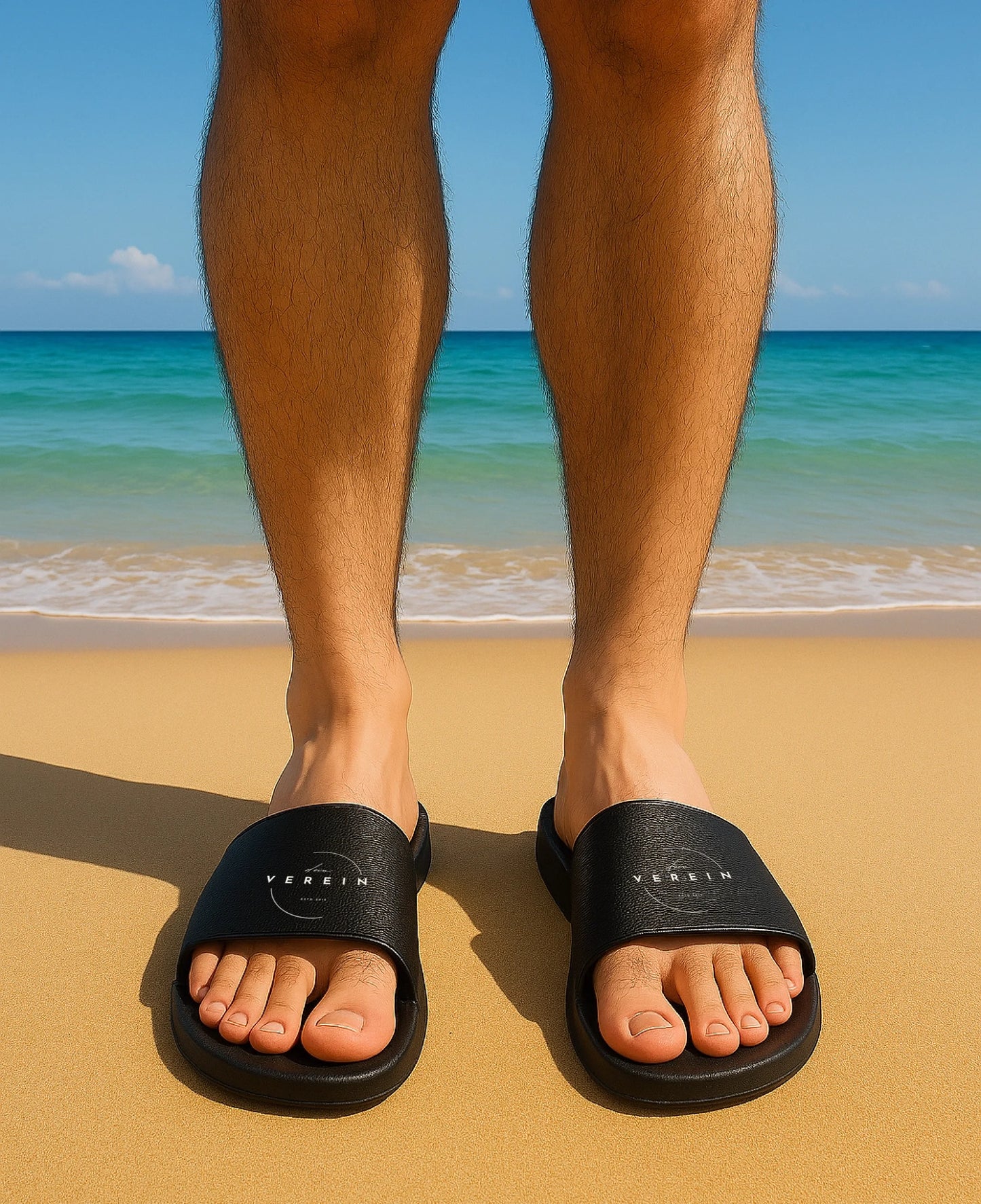 Schwarze Badelatschen mit breitem Riemen. Auf beiden Riemen ist in weißen Buchstaben der Schriftzug ‚dein Verein‘ aufgedruckt. Der Text kann individuell mit dem eigenen Bandnamen gestaltet werden.