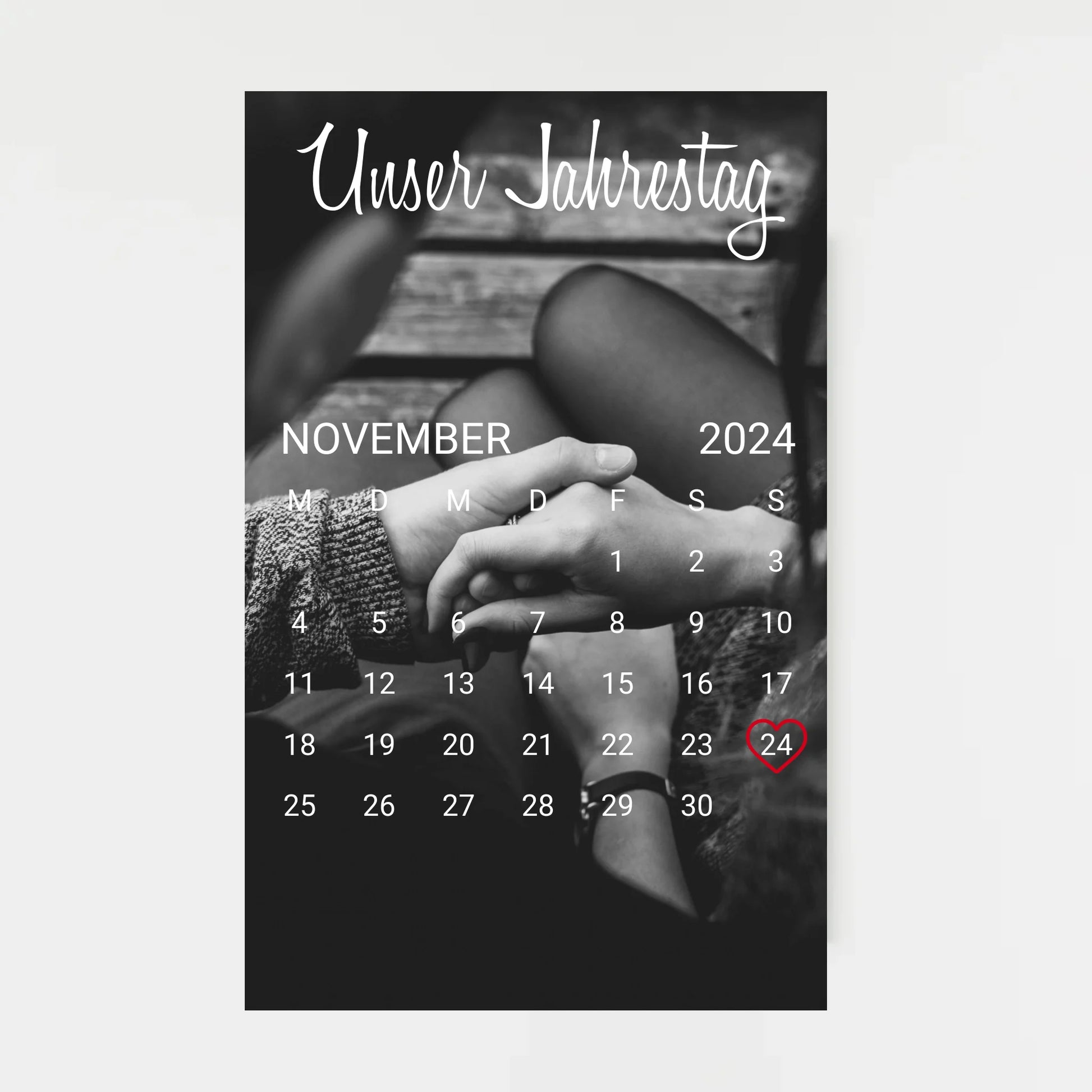Poster im Kalender-Design mit schwarz-weißem Hintergrundfoto, hier als Beispiel zwei sich haltende Hände. Oben die feste Überschrift ‚Unser Jahrestag‘. Monat, Jahr und Tag sind personalisierbar, der ausgewählte Tag wird mit einem Herz markiert. Hintergrundfoto ist ebenfalls personalisierbar.
