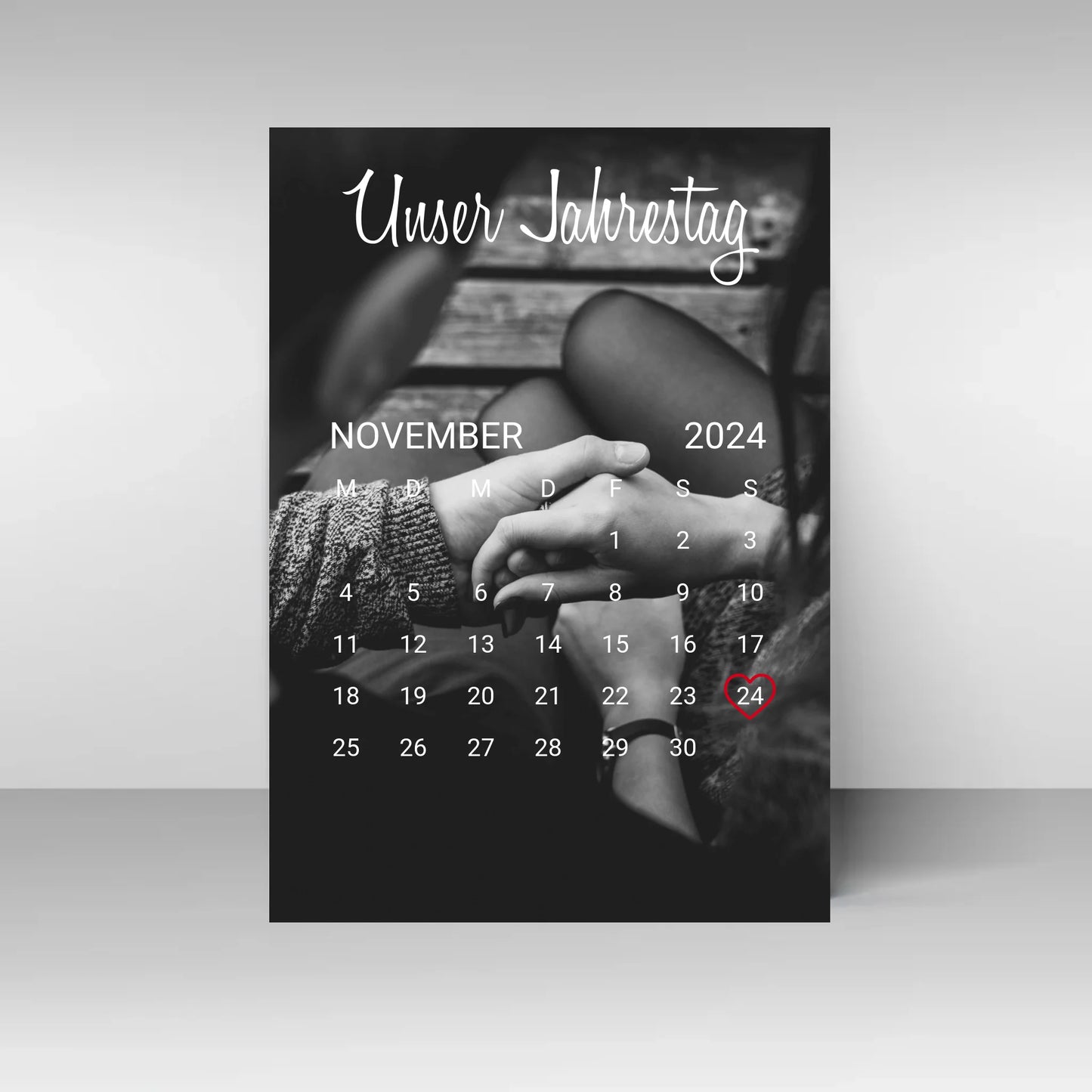 Poster im Kalender-Design mit schwarz-weißem Hintergrundfoto, hier als Beispiel zwei sich haltende Hände. Oben die feste Überschrift ‚Unser Jahrestag‘. Monat, Jahr und Tag sind personalisierbar, der ausgewählte Tag wird mit einem Herz markiert. Hintergrundfoto ist ebenfalls personalisierbar.