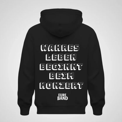Schwarzer Hoodie mit großem weißen Schriftzug auf der Rückseite: ‚Wahres Leben beginnt beim Konzert‘. Darunter steht der Schriftzug ‚Eure Band‘. Der Bandname kann individuell angepasst werden.